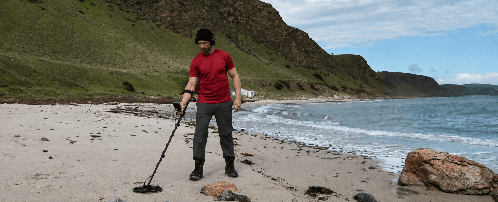 Hombre con audífonos buscando monedas en una playa de arena con el Detector de metales Minelab Equinox 700.