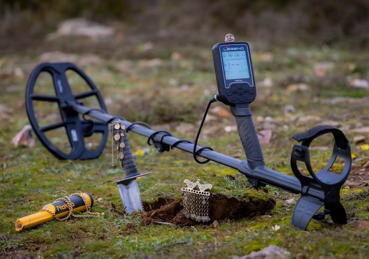 Equipo completo del Detector de metales Nokta The Legend Pro Pack junto a un pozo de excavación con reliquias descubiertas.