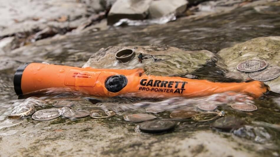 Primer plano del Garrett Pro Pointer AT Pinpointer naranja sumergido parcialmente en el agua de un río.