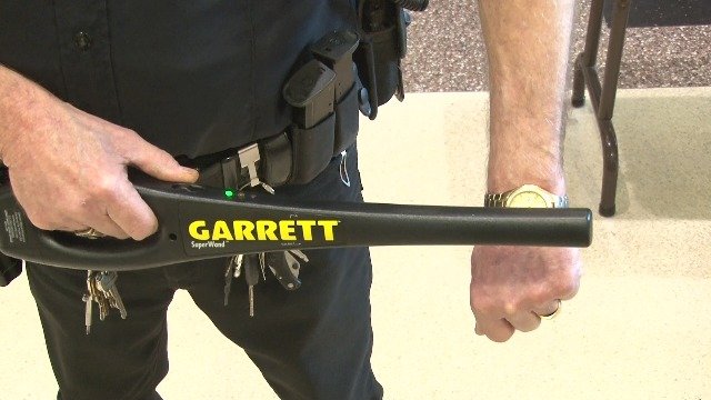 Oficial utilizando el detector de metales manual Garrett SuperWand para escanear el brazo de una persona.