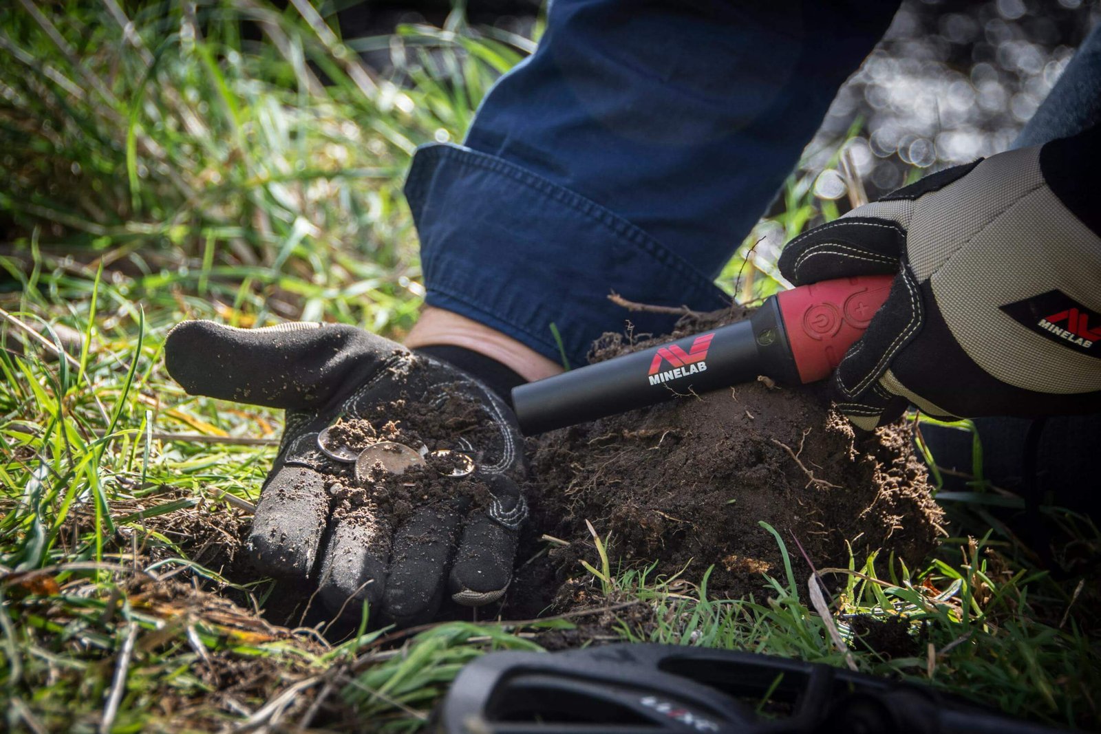 Operador utilizando el localizador Minelab Pro Find 40 para revisar un terrón de tierra con monedas.