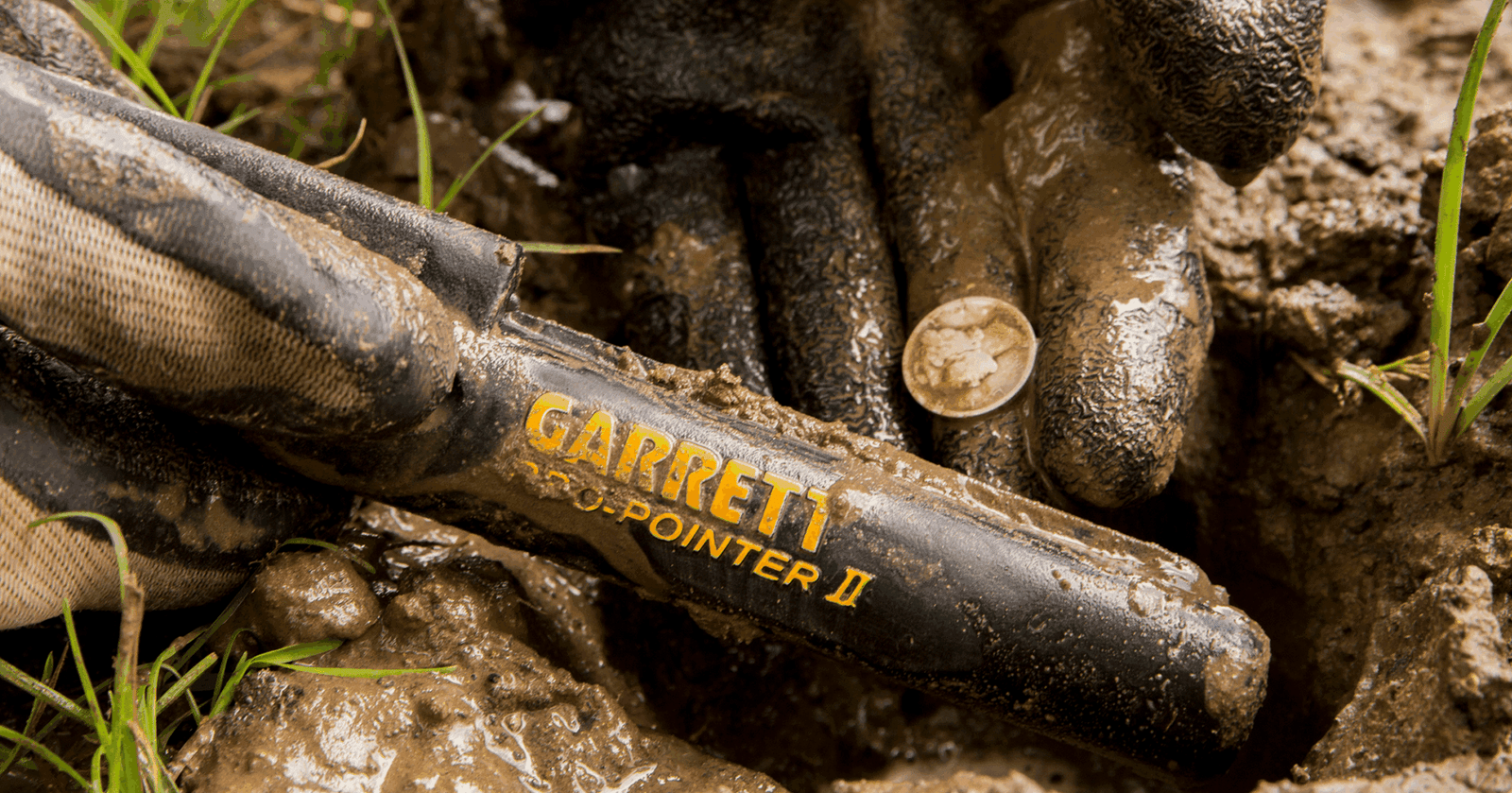 Operador con guantes de seguridad usando el Garrett Pro Pointer 2 en un terreno de lodo húmedo.