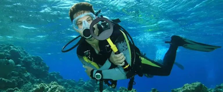 Buzo sumergido sosteniendo el Nokta PulseDive Scuba Pinpointer Amarillo en un arrecife de coral bajo el agua.