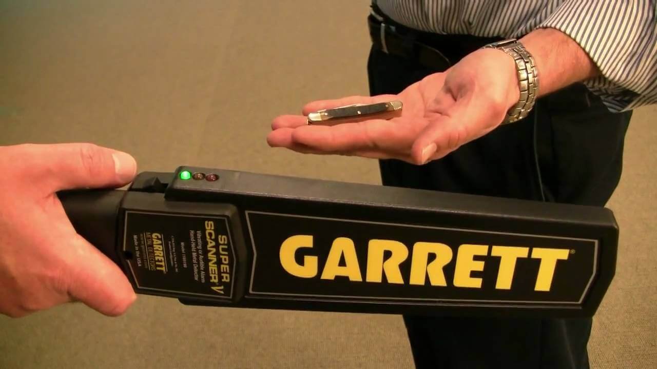 Demostración técnica del Garrett SuperScanner V detectando una navaja pequeña sobre la mano de un usuario.