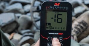 Detector de metales Minelab Vanquish siendo utilizado para buscar objetos de valor en el suelo húmedo de un río.
