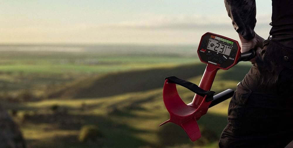 Operador sosteniendo el Detector de metales Minelab Vanquish 440 con detalles rojos en un prado abierto.