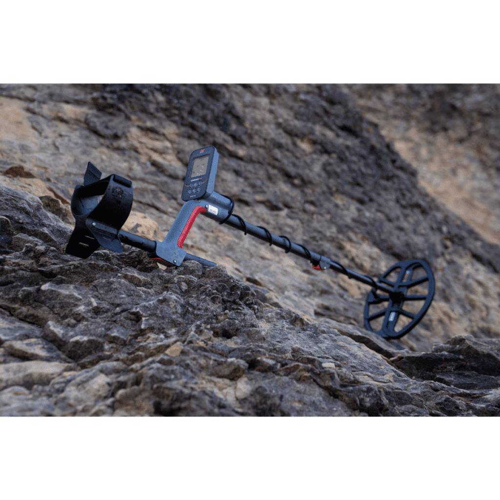 Detector de metales Minelab Vanquish 360 mostrando su bobina DD impermeable sobre un terreno de tierra y pasto seco.